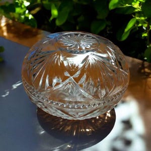 May include: A clear glass bowl with a geometric pattern. The bowl is round and has a lid. The bowl is sitting on a white surface.