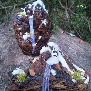 May include: Two miniature woodland scenes made from driftwood, moss, and white paint. Each scene features a small waterfall and a deer figurine.