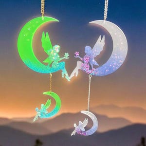 May include: Three crescent moon charms with glitter accents and fairy silhouettes. The moons are green, white, and purple. The fairies are holding stars.