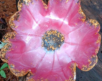 May include: A pink resin flower-shaped bowl with gold leaf accents. The bowl has a white center and a wavy edge.