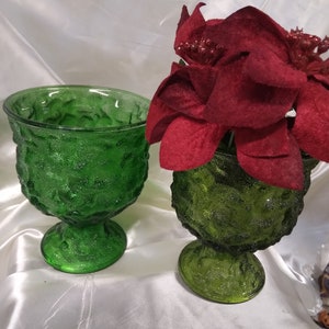 May include: Two green glass pedestal bowls featuring a textured, pebbled surface. One bowl is empty, while the other contains a cluster of deep red artificial poinsettia flowers with glittery accents on the petals, creating a festive display.