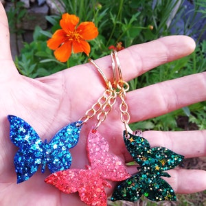 May include: Three gold keychains with glitter butterfly charms. The butterflies are blue, red, and green.