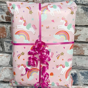May include: A pink gift bag with a unicorn and rainbow pattern. The bag is tied with a pink ribbon.
