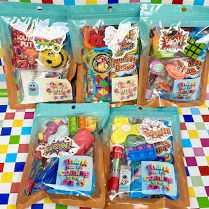 May include: Five clear plastic bags filled with colourful party favours. Each bag contains various toys, sweets, and stickers. The bags have labels with phrases like "Thank you for coming to my party" and comic book-style sound effects.