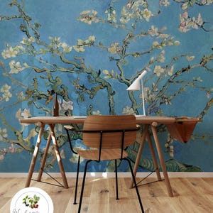 Puede incluir: Un escritorio de madera con una silla de metal negro delante. La pared detrás del escritorio está cubierta con un papel tapiz floral azul y blanco con una pintura de una rama de árbol en flor.