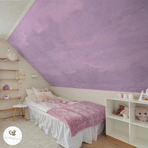 May include: A bedroom featuring a lavender wall and a bed with a pink blanket and white bedding. A white shelf displays stuffed toys and candles. A small side table and a wooden shelf are also present.