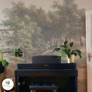 Puede incluir: Un piano digital negro con el logotipo de Yamaha, situado delante de un mural de pared que representa una escena de bosque con árboles y colinas. El piano tiene un banco negro y unos auriculares.