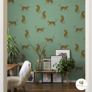 以下が含まれることがあります： ヒョウ柄のデカールで飾られた緑色の壁のある部屋。木製のベンチには額入りのアートワークと植物が置かれています。白くふわふわの椅子が木製のテーブルの近くにあります。部屋は自然でボヘミアンな美学を持っています。