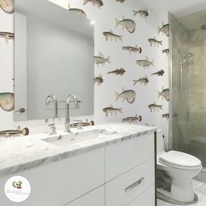 May include: A modern bathroom with a white vanity, marble countertop, and a large mirror. The walls are adorned with a repeating pattern of various fish illustrations. A glass shower and a white toilet complete the space, creating a fresh and aquatic theme.