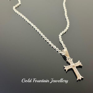 May include: A silver chain necklace with a small, silver cross pendant. The cross is decorated with small, clear stones.