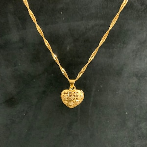 May include: A gold chain necklace with a heart-shaped pendant. The pendant has a detailed, textured design.