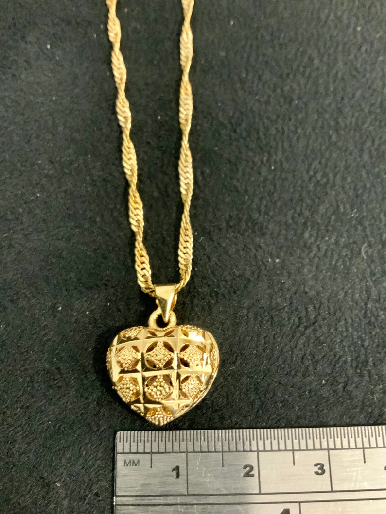 May include: A gold heart-shaped pendant necklace with a detailed, intricate design. The pendant is approximately 2.5 cm in diameter. The chain is a twisted rope style.