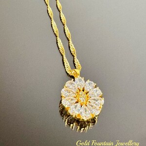 以下が含まれることがあります： 丸いデザインのペンダントがついた、金のチェーンネックレス。ペンダントは、小さな透明な石で囲まれています。チェーンはねじれたロープスタイルです。画像の下部に「Gold Fountain Jewellery」というテキストが表示されています。