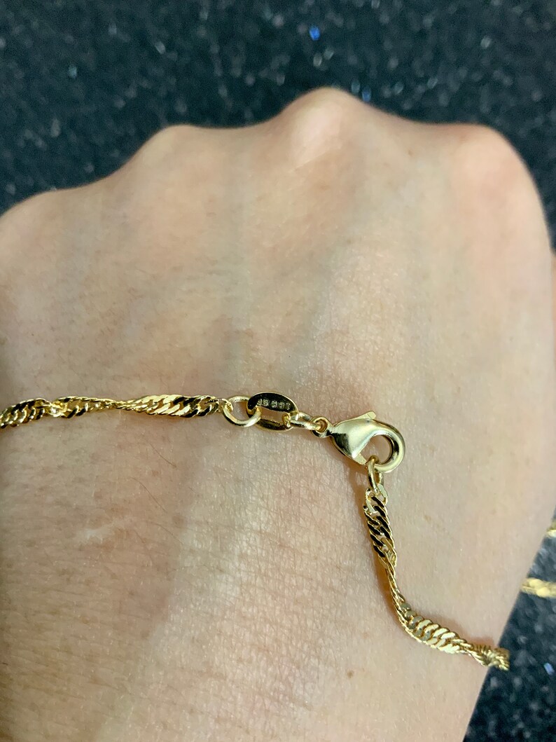 May include: A gold chain necklace with a twisted rope design. The chain has a lobster clasp closure. The chain is on a person's wrist.