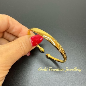 May include: A gold bangle bracelet with a floral design. The bracelet is open and has a simple, elegant design.