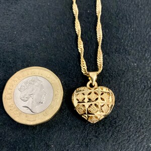 May include: A gold chain necklace with a heart-shaped pendant. The pendant has a detailed, intricate design.