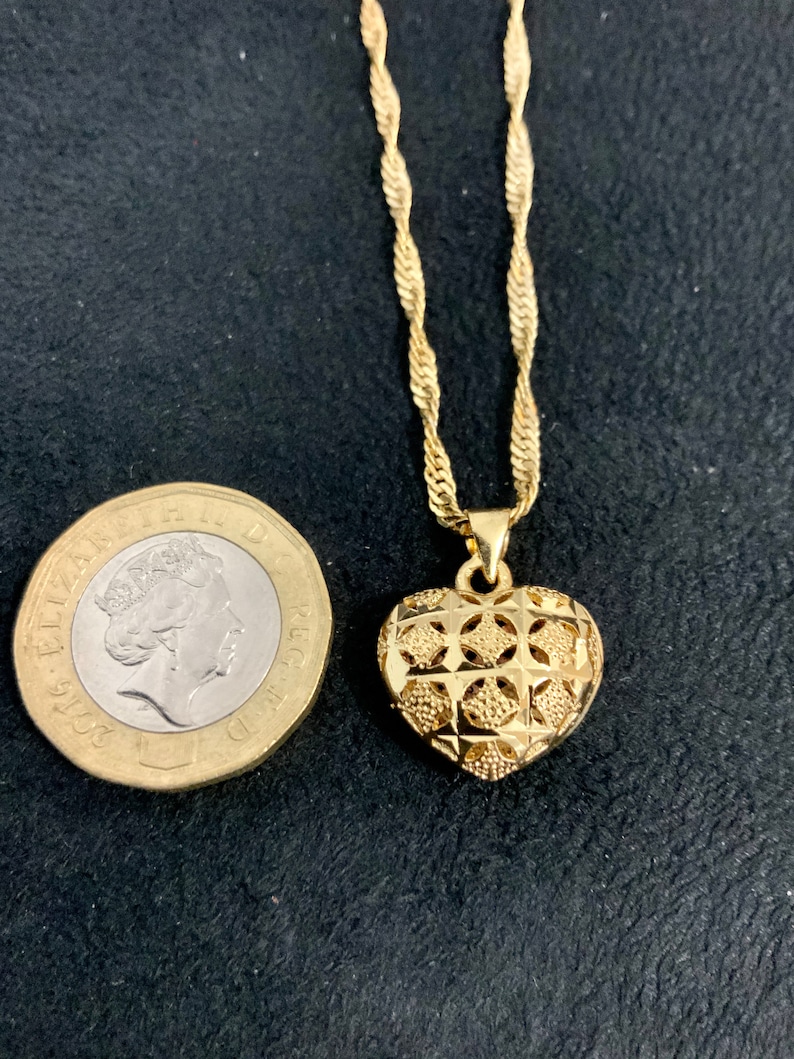May include: A gold chain necklace with a heart-shaped pendant. The pendant has a detailed, intricate design.