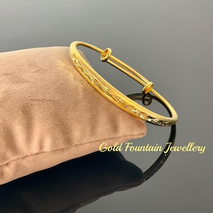 May include: A gold bangle bracelet with a textured design. The bracelet is open and has a hinge closure.