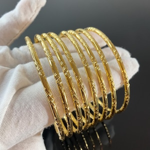 May include: A set of eight gold-coloured bangles with a textured design. The bangles are stacked on top of each other.