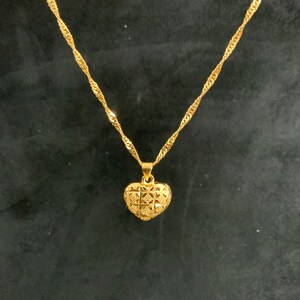 May include: A gold chain necklace with a heart-shaped pendant. The pendant has a detailed, textured design.