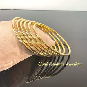 May include: A set of eight gold bangles stacked on top of each other. The bangles are smooth and shiny. The text "Gold Fountain Jewellery" is visible at the bottom of the image.