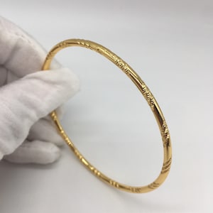 May include: A gold bangle bracelet with a textured design. The bracelet is simple and elegant.