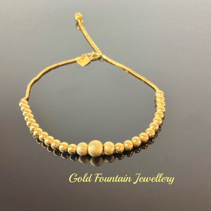 May include: A gold beaded bracelet with a heart-shaped clasp and a textured centre bead. The bracelet is adjustable and has a delicate chain.