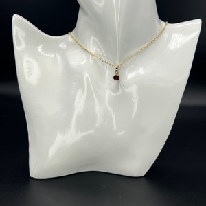 May include: A gold chain necklace with a small, round, dark red gemstone pendant.