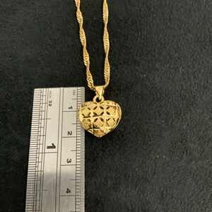 May include: A gold chain necklace with a heart-shaped pendant. The pendant has a detailed, intricate design and is approximately 2.5 cm in diameter.