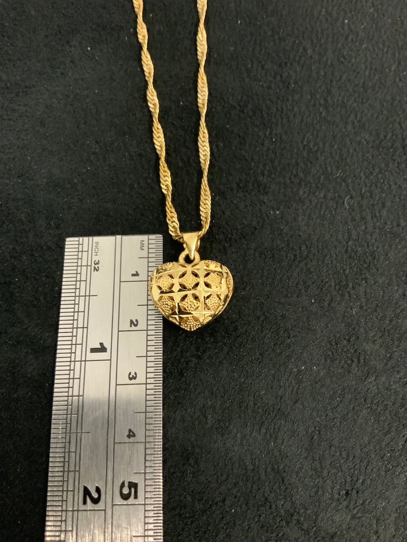 May include: A gold chain necklace with a heart-shaped pendant. The pendant has a detailed, intricate design and is approximately 2.5 cm in diameter.