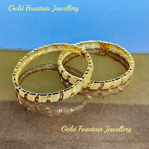 May include: Two gold bangles with a textured design. The bangles are stacked on top of each other. The text "Gold Fountain Jewellery" is visible at the top and bottom of the image.