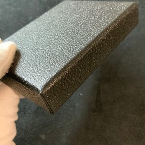 May include: A black square box with a textured surface. The box is made of a sturdy material and has a smooth, even finish.