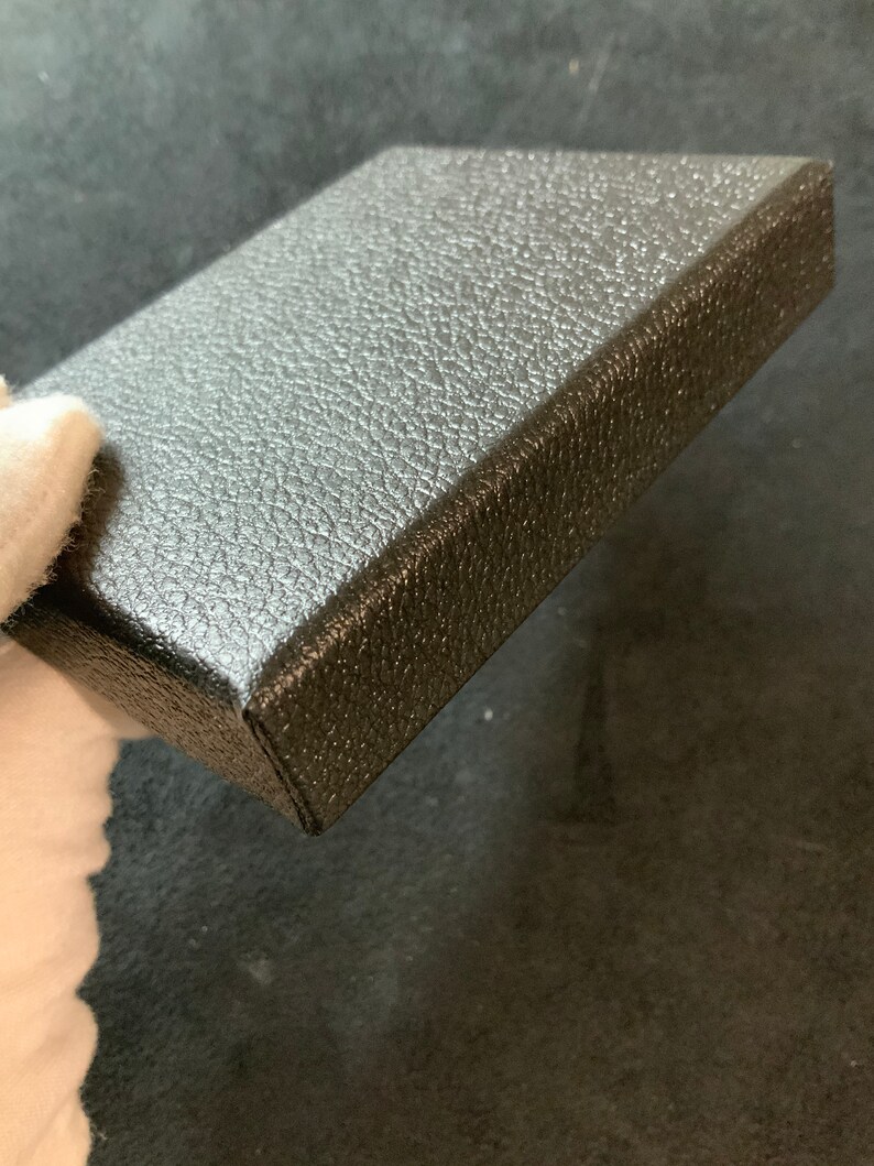 May include: A black square box with a textured surface. The box is made of a sturdy material and has a smooth, even finish.