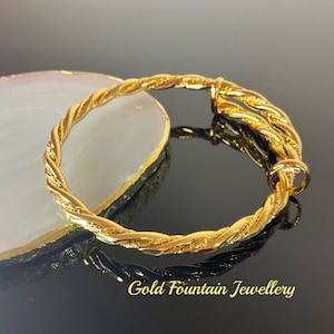 May include: A gold-toned twisted bangle bracelet with a hinged clasp. The bracelet is on a white surface with a black background.