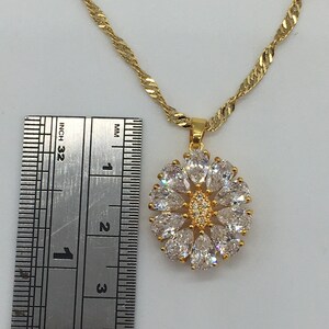 以下が含まれることがあります： クリアなキュービックジルコニアの石がついた花のデザインのペンダントが付いたゴールドチェーンネックレス