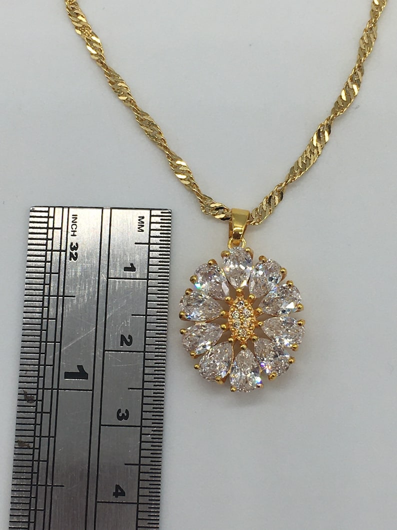 以下が含まれることがあります： クリアなキュービックジルコニアの石がついた花のデザインのペンダントが付いたゴールドチェーンネックレス