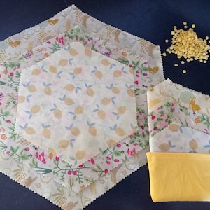 Peut inclure: Ensemble de quatre emballages alimentaires en cire d'abeille avec différents motifs floraux et géométriques. Les emballages sont empilés les uns sur les autres et sont entourés de pastilles de cire d'abeille jaunes. Les emballages sont emballés dans une pochette en tissu jaune.