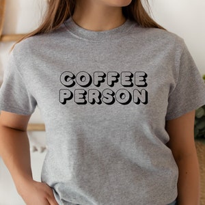 May include: A gray t-shirt with the text "COFFEE PERSON" in black, 3D-style lettering.