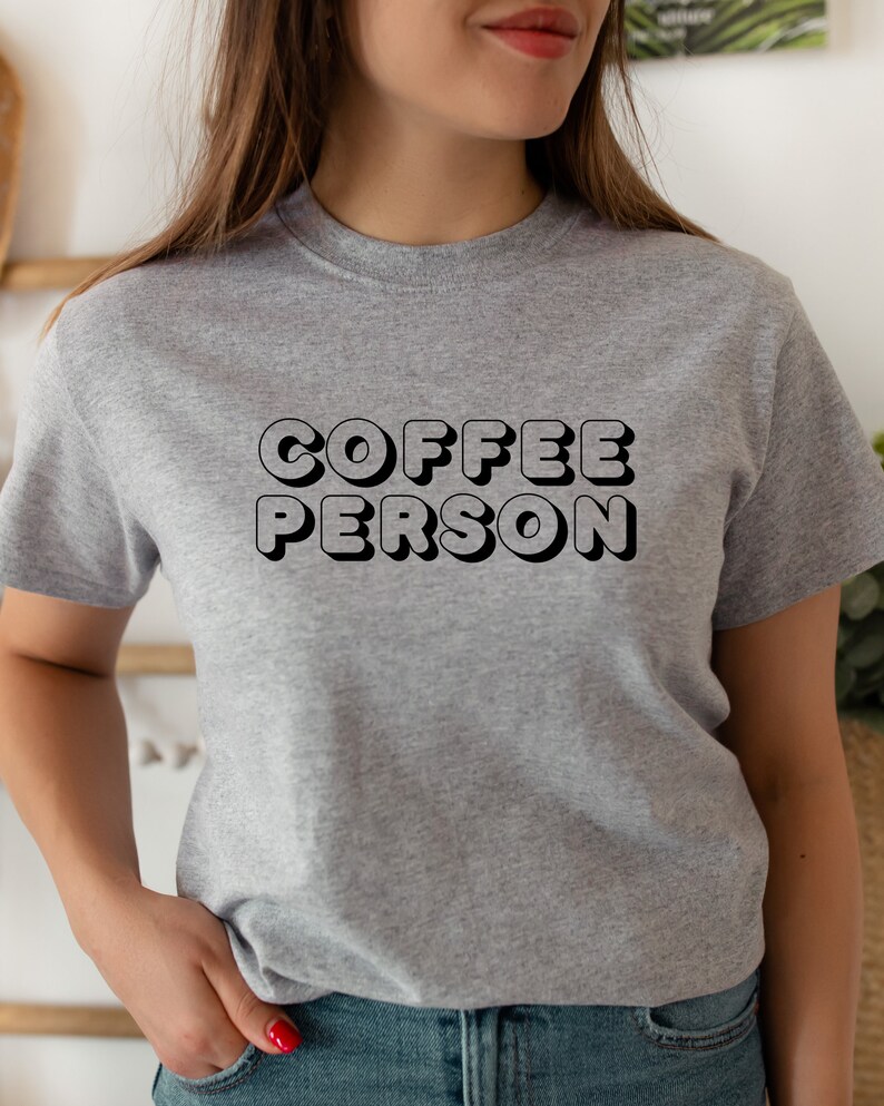May include: A gray t-shirt with the text "COFFEE PERSON" in black, 3D-style lettering.