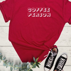 May include: Red t-shirt with white text that reads "COFFEE PERSON" in a retro font.