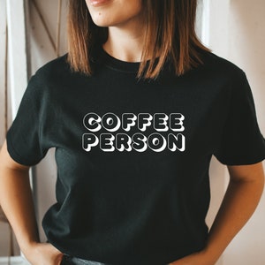 May include: A black t-shirt with white text that reads "COFFEE PERSON" in a retro style font.