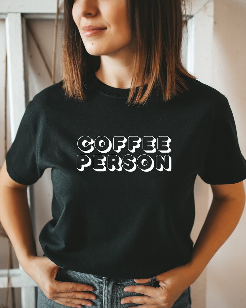 May include: A black t-shirt with white text that reads "COFFEE PERSON" in a retro style font.