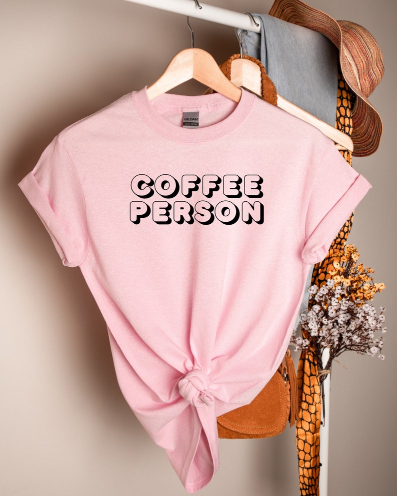 May include: Pink t-shirt with black text that reads "COFFEE PERSON" in a retro style font.