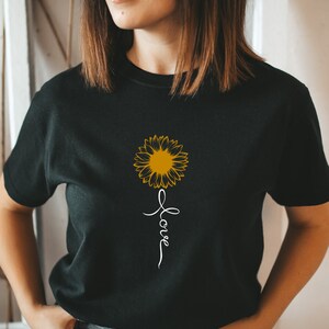 Puede incluir: Camiseta negra con un gráfico de girasol amarillo y la palabra "love" escrita verticalmente debajo.