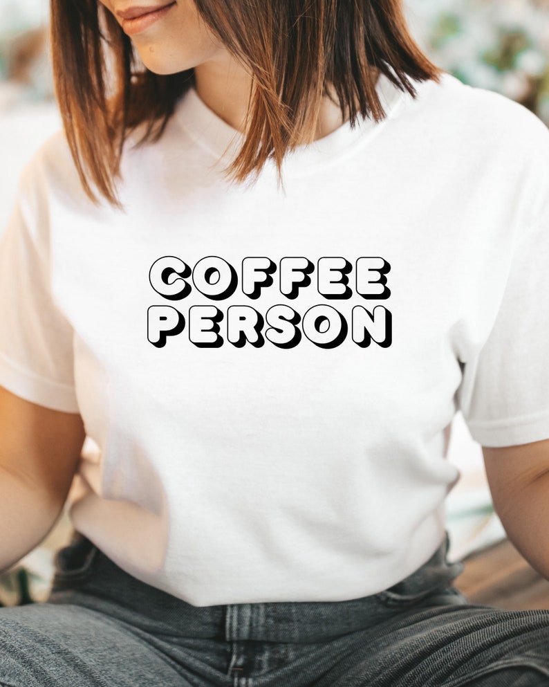 May include: White t-shirt with the text "COFFEE PERSON" in black, 3D-style lettering.