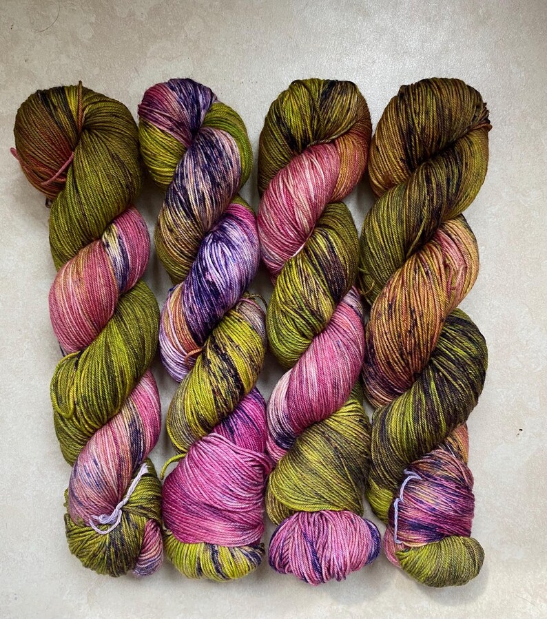 Op de afbeelding: Vier bollen garen in een gem&ecirc;leerde kleur met tinten van groen, roze, paars en bruin.