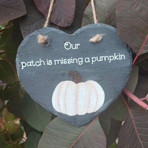 May include: A heart-shaped slate sign with the text "Our patch is missing a pumpkin" and a white painted pumpkin with a brown stem.