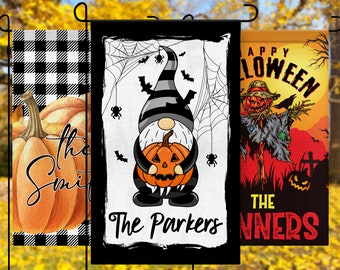 May include: Three Halloween-themed garden flags with different designs. The first flag features a black and white checkered pattern with a large orange pumpkin in the center. The second flag has a black and white gnome holding a pumpkin with a spiderweb and bats in the background. The third flag has a red and orange background with a scarecrow and the text "Happy Halloween The Winners".
