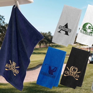 May include: Five rectangular golf towels in navy blue, white, and black, featuring embroidered names and golf-themed graphics. The navy towel displays the name Richard with crossed clubs, while others show names like Anthony, Samuel, Christian, and Charles.