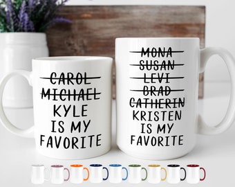 Puede incluir: Dos tazas de cerámica blanca con texto negro. La taza de la izquierda dice "CAROL MICHAEL KYLE IS MY FAVORITE". La taza de la derecha dice "MONA SUSAN LEVI BRAD CATHERIN KRISTEN IS MY FAVORITE".